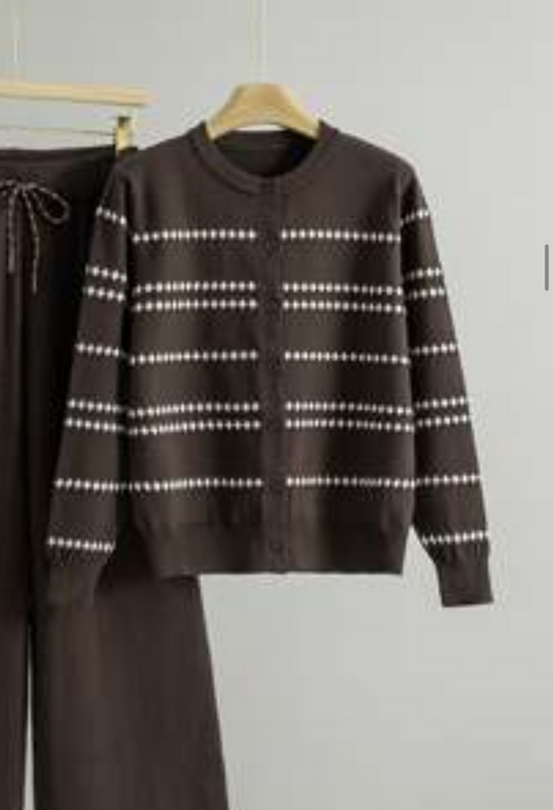 A dark brown knit sweater with white dotted horizontal stripes hanging on a wooden hanger against a light gray wall, with matching dark brown pants partially visible on the left.